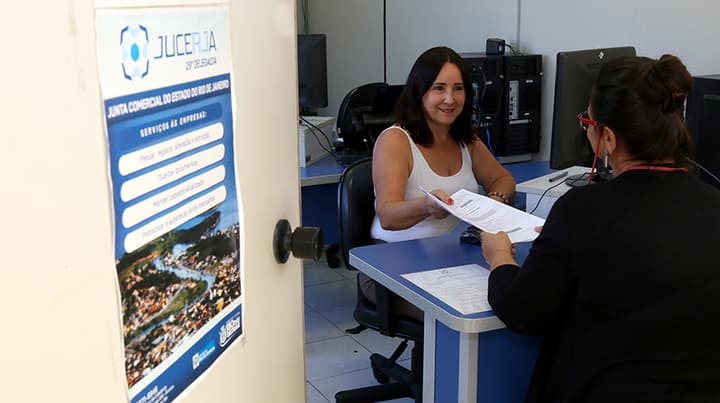 Funcionária da Jucerja entregando documento para uma cidadã